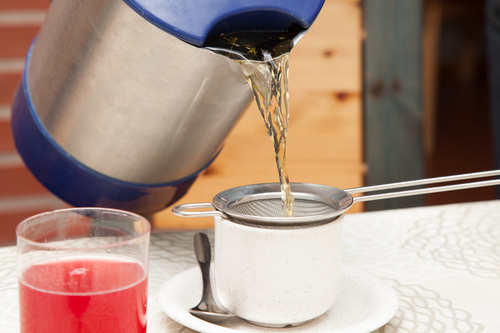 Juomalasissa punaista mehua ja vesipannusta kaadetaan kuumaa vettä kuppiin.