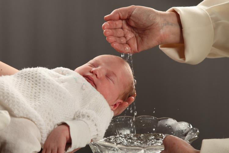 Pappi valelee vettä kastepukuisen lapsen päähän