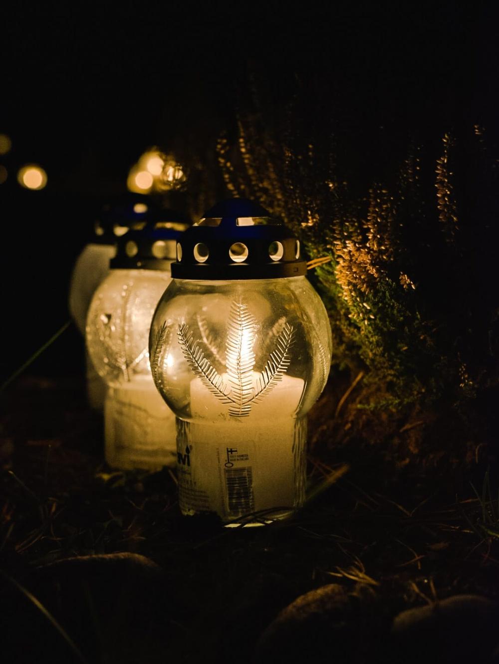 Kynttilälyhtyjä sytytettyinä pimeässä illassa, taustalla havuja ja valopisteitä