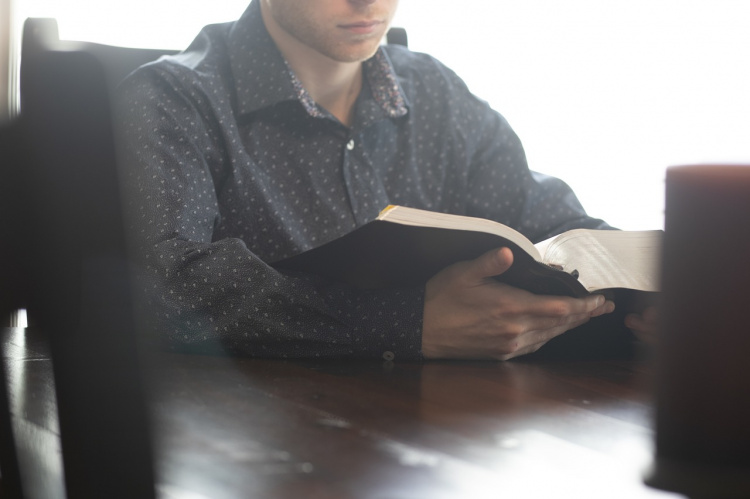 Mies pöydän ääressä lukee Raamattua