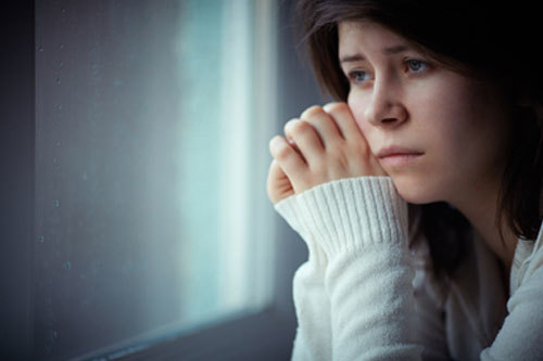 Surullisen näköinen nainen katselee ikkunasta kädet liitettyinä yhteen poskelle
