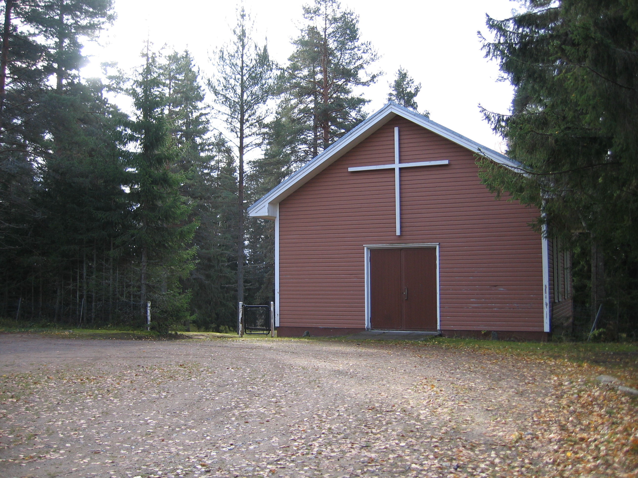 Kuvassa hautausmaan portilla sijaitseva rakennus, jonka oven päällä iso valkoinen risti